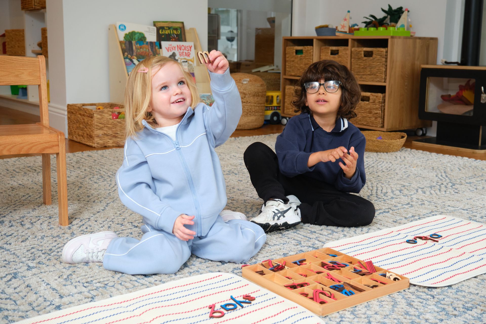 Two children in hats playing with a toy truck and sand in a sandbox.