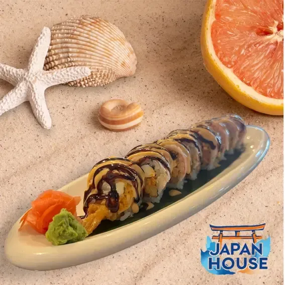 Sushi roll on a plate with wasabi and ginger, beside a starfish, shell, and grapefruit slice on sand background