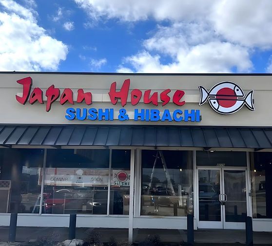 Storefront sign for Japan House Sushi & Hibachi with red and blue lettering under a cloudy sky