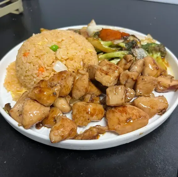 Plate of fried rice, glazed chicken cubes, and mixed vegetables on a dark table