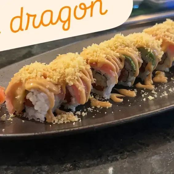 Sushi rolls topped with sauce and crunchy crumbs on a black plate, with “dragon” text above them
