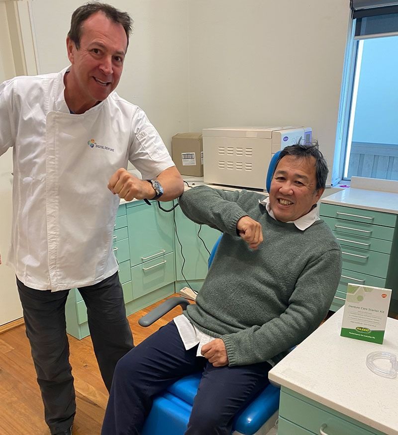 A man and a person in a medical setting bump elbows — My Denture Clinic in Benowa, QLD
