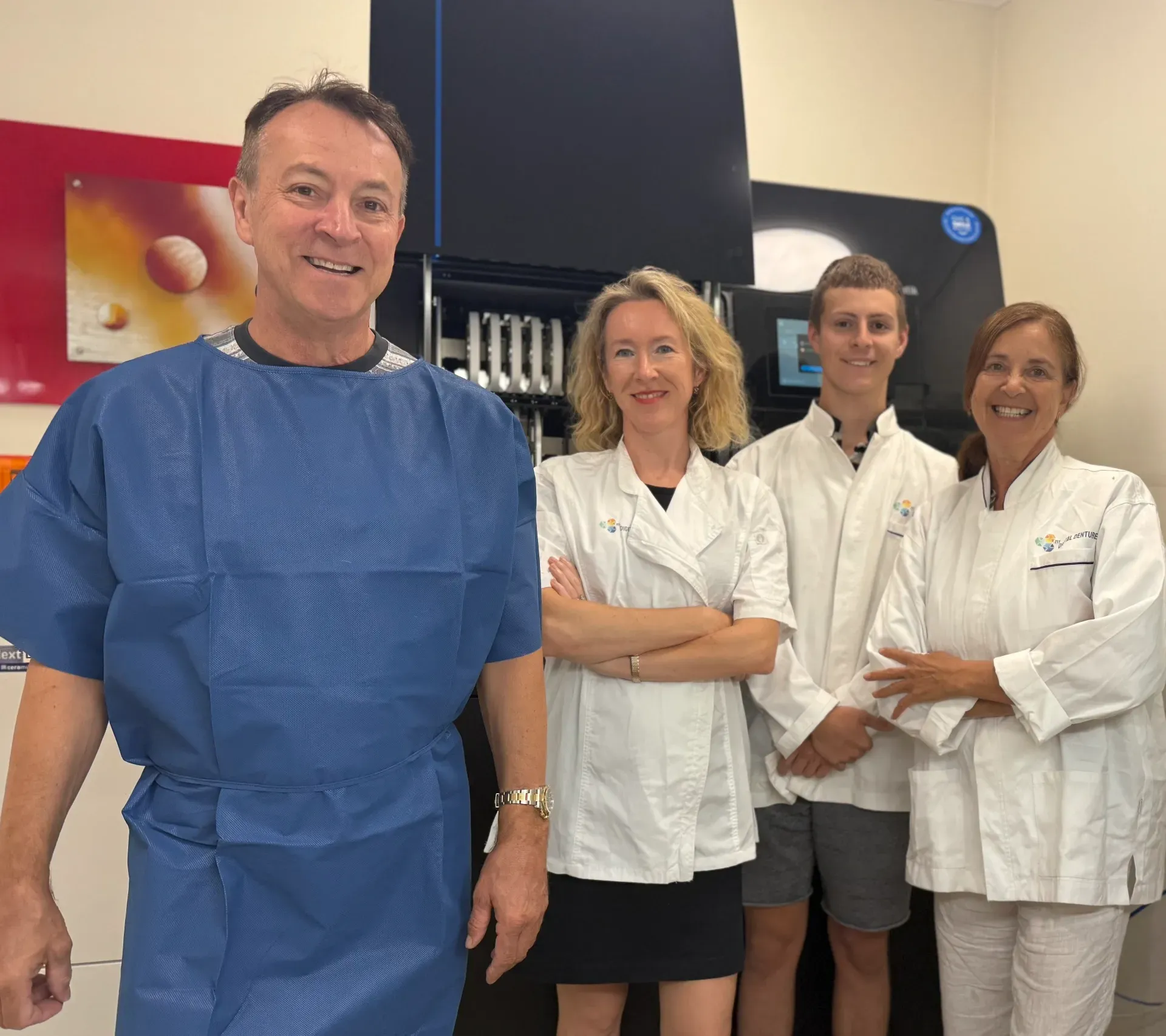 Four medical staff in white coats stand with a man in blue scrubs in a clinic or lab. — My Denture Clinic in Benowa, QLD