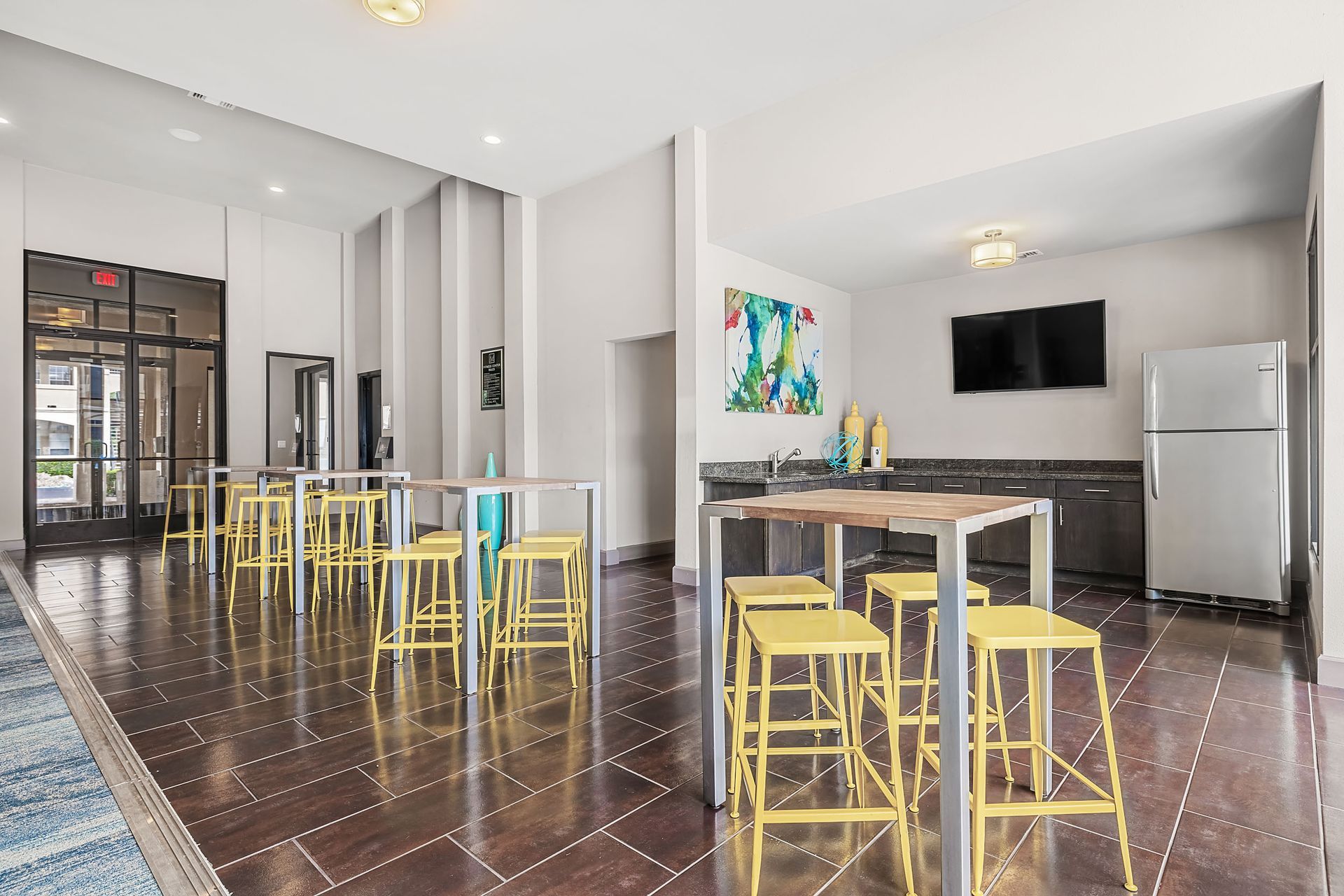 Modern kitchen-dining area with glass table, yellow stools, stainless appliances, and dark wood floors