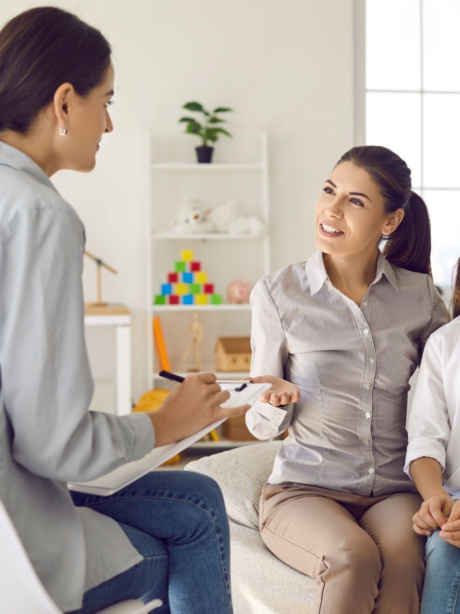 A woman is sitting on a couch with two children and talking to a doctor.