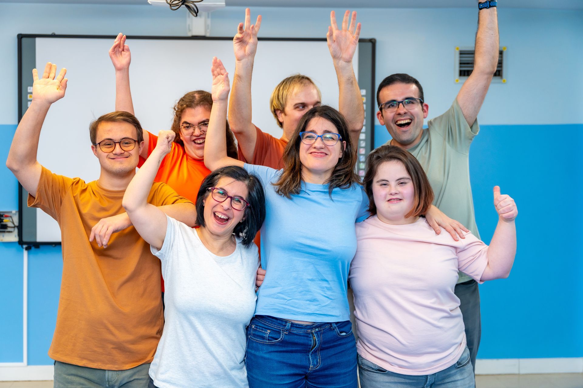 A group of people with disabilities are posing for a picture with their hands in the air.