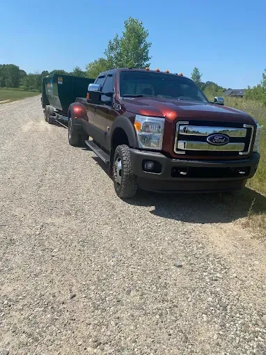 Red Ford truck towing a green trailer on a gravel road under a bright blue sky.