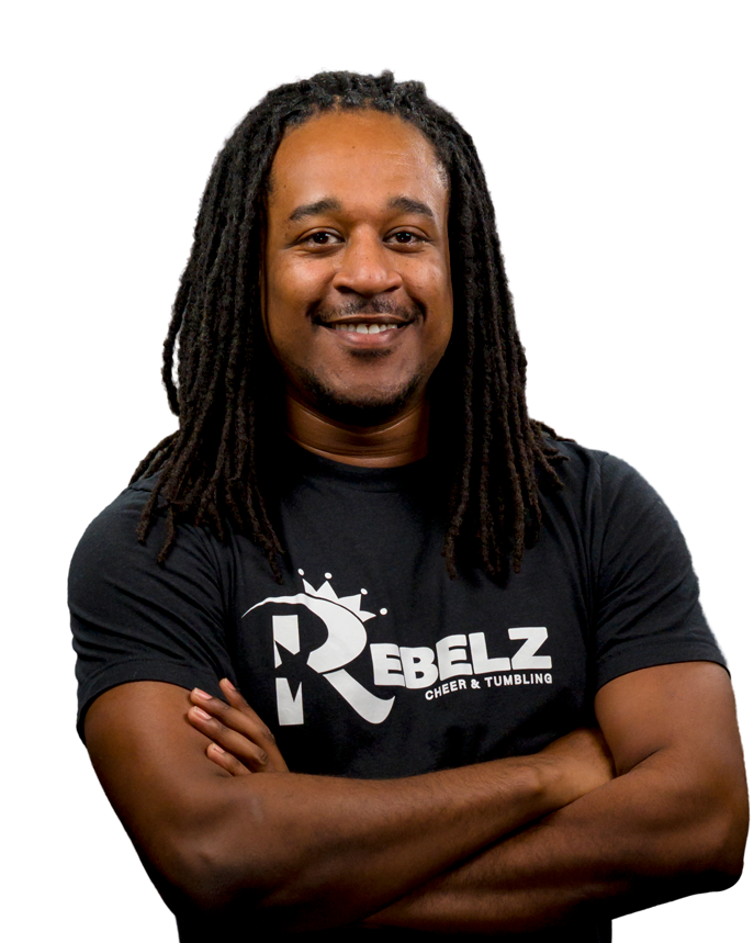 A man with dreadlocks is smiling with his arms crossed