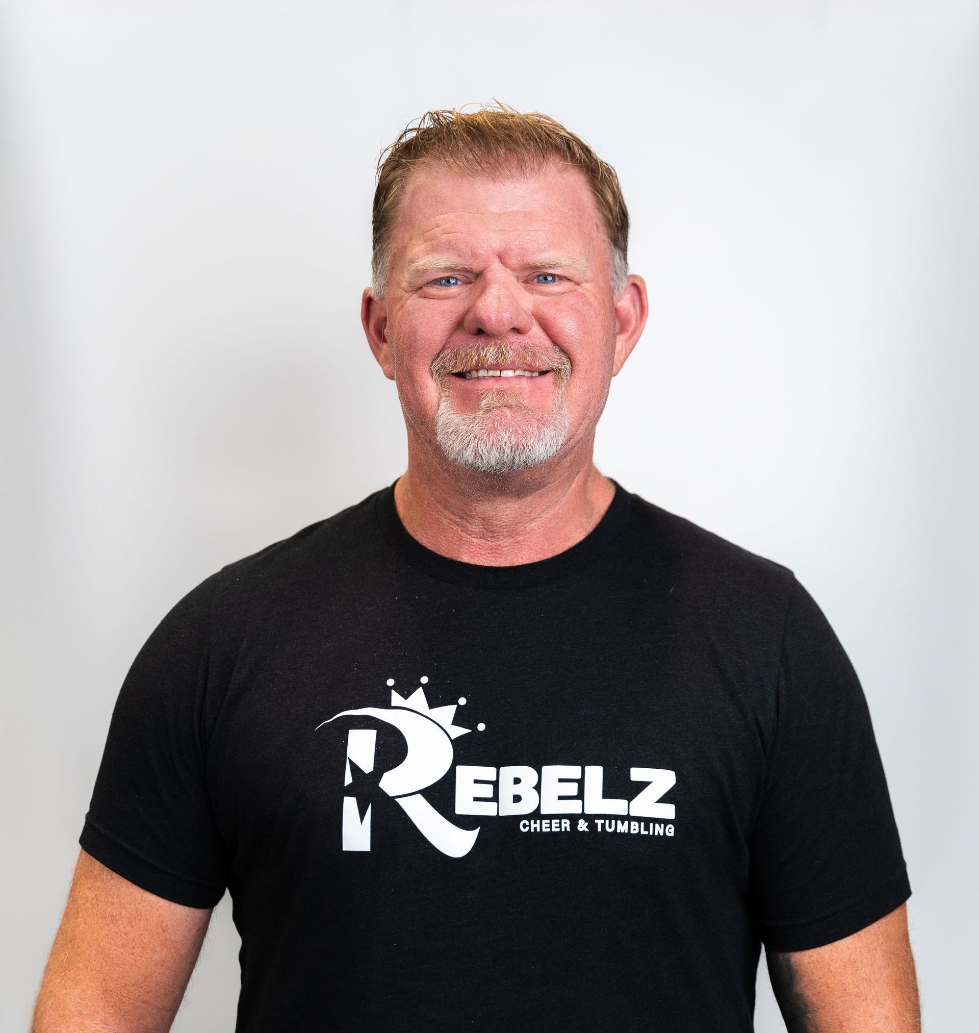 A man in a black shirt with his arms crossed is smiling.