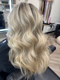 Woman with long, wavy blonde hair styled in a salon, sitting in a chair.