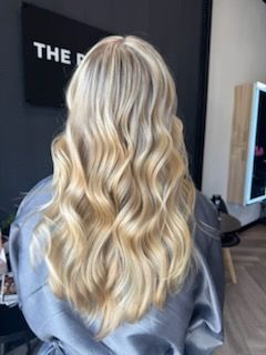 Woman with long, wavy blonde hair, styled in a salon setting.