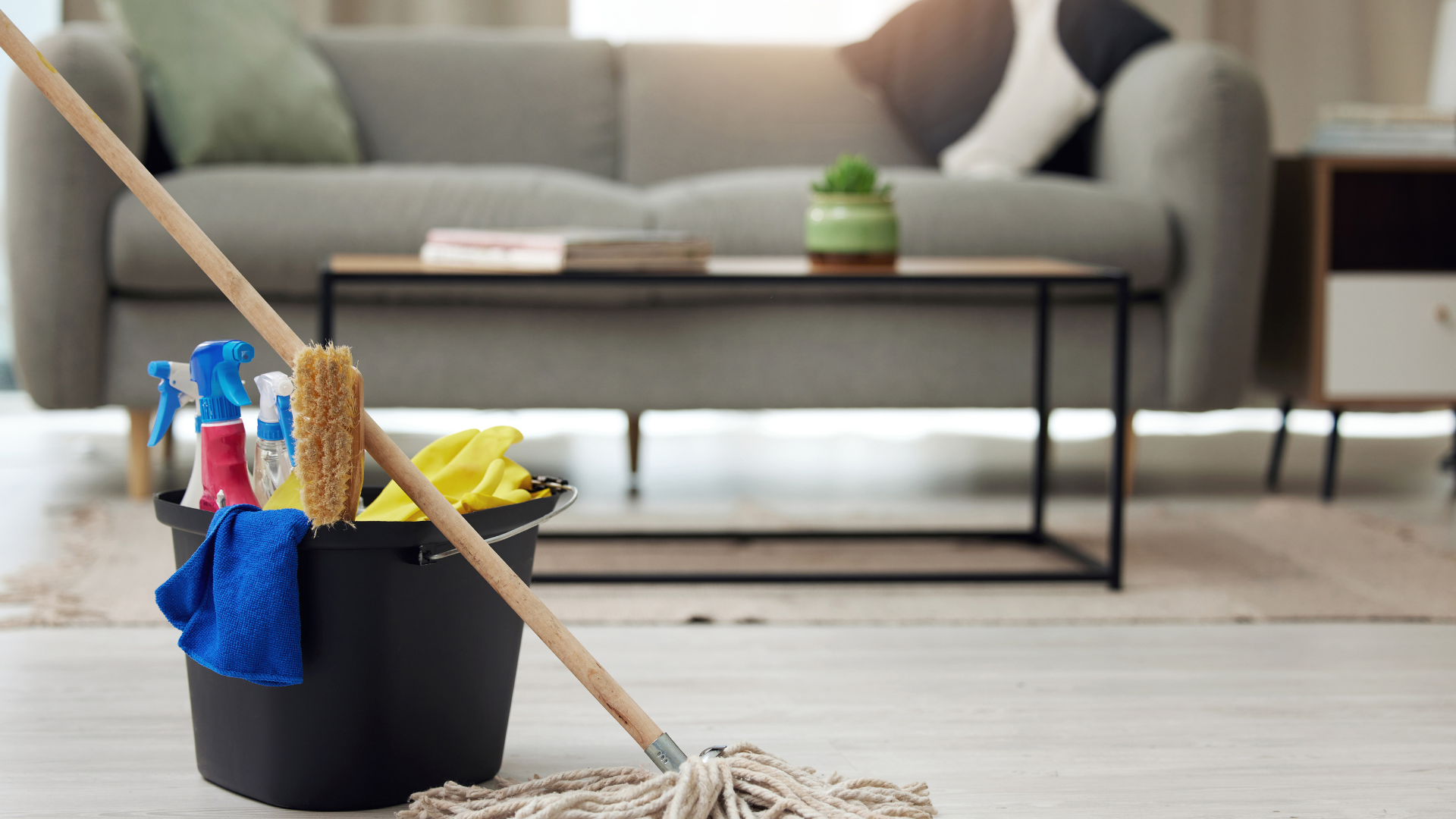 A mop is sitting next to a bucket of cleaning supplies in a living room.