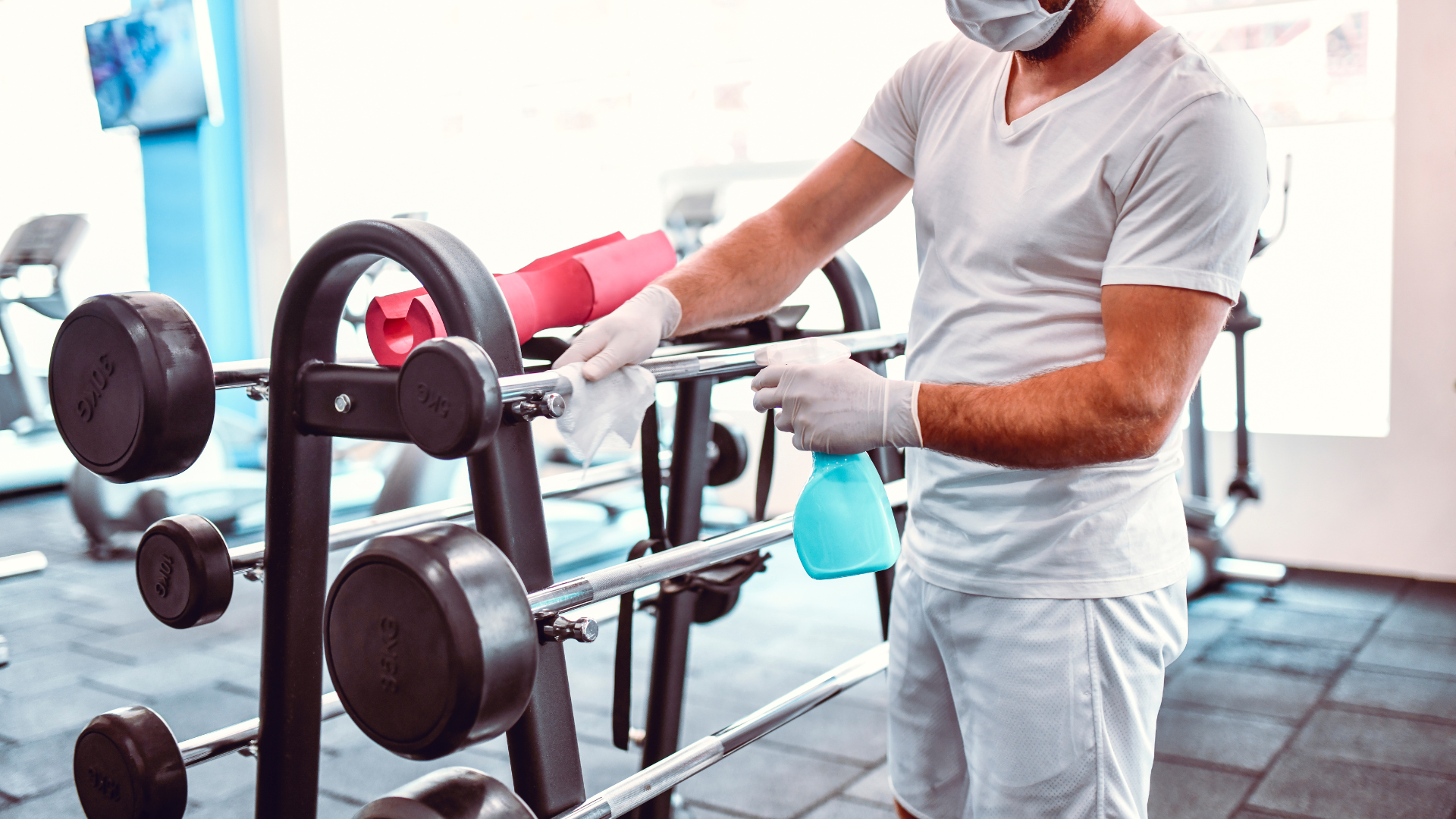 A man wearing a mask and gloves is cleaning a gym.