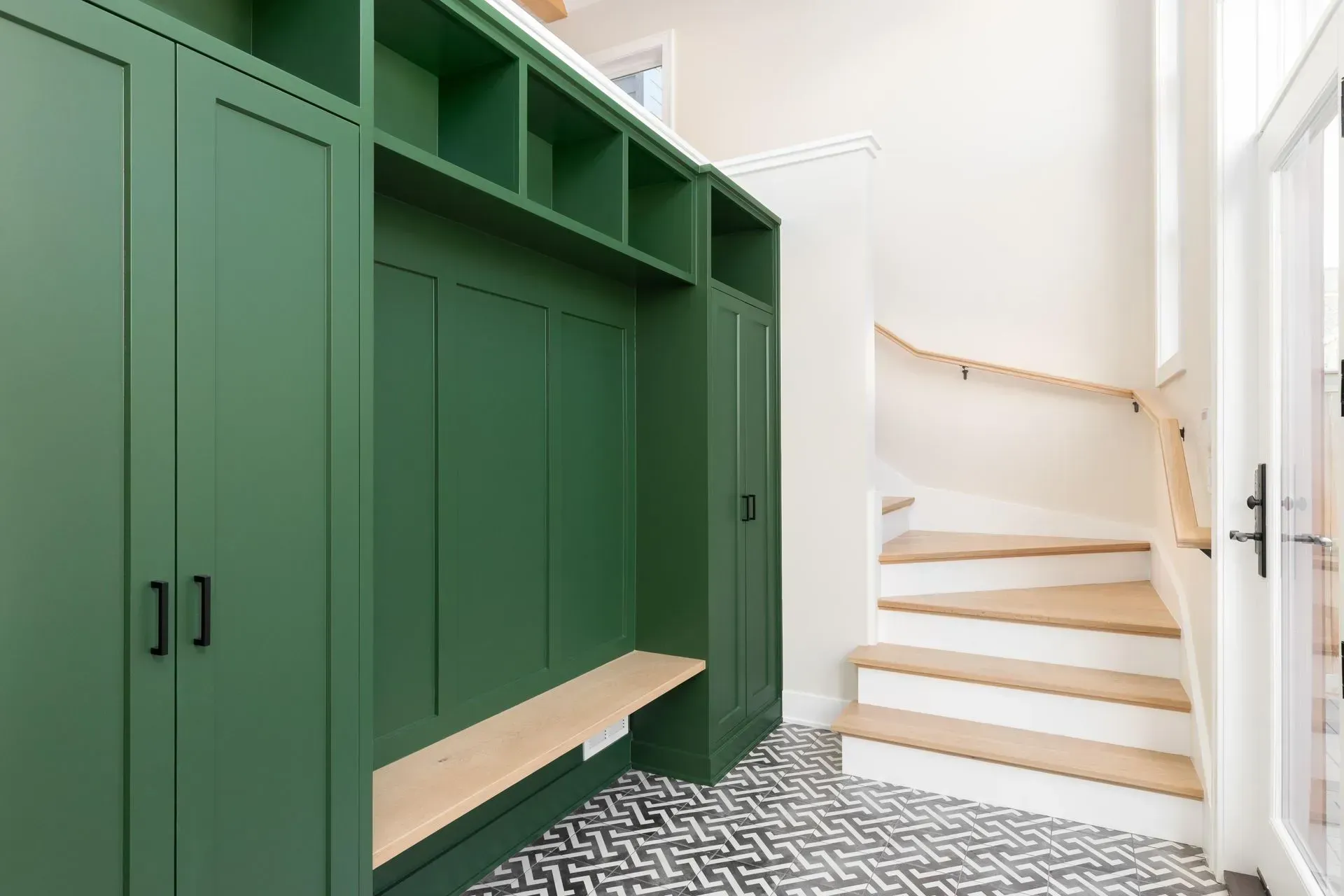 A mud room with green cabinets and white stairs.