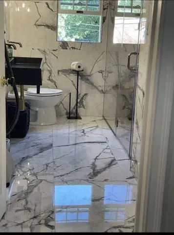 A bathroom with marble floors , a toilet , sink and shower.