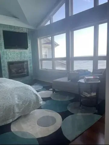 A bedroom with a bed , fireplace , television and lots of windows.