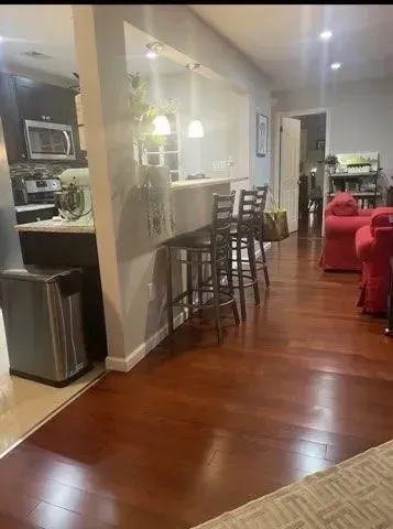 A living room with hardwood floors and a kitchen in the background.