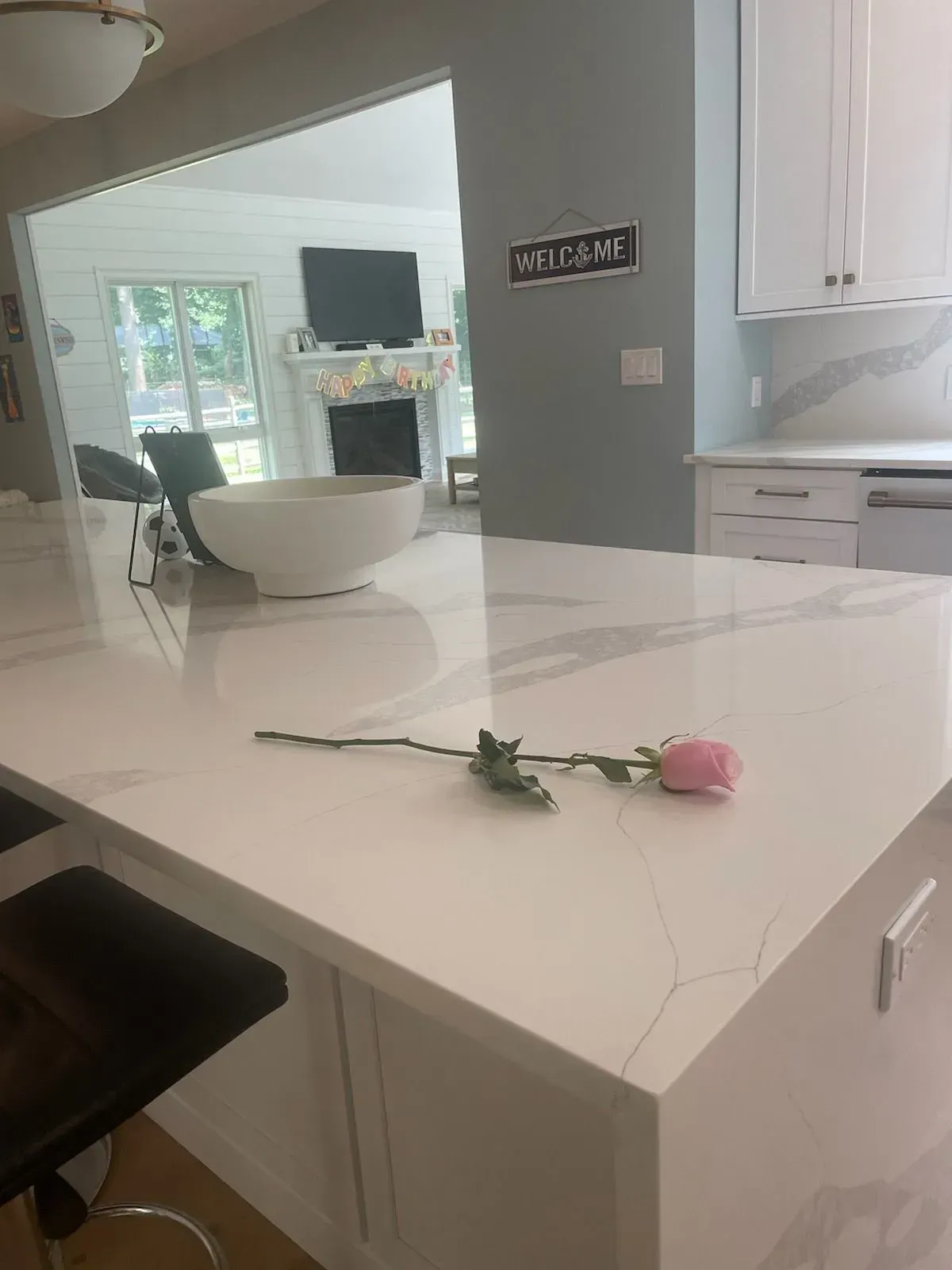 A pink rose is sitting on top of a white counter in a kitchen.