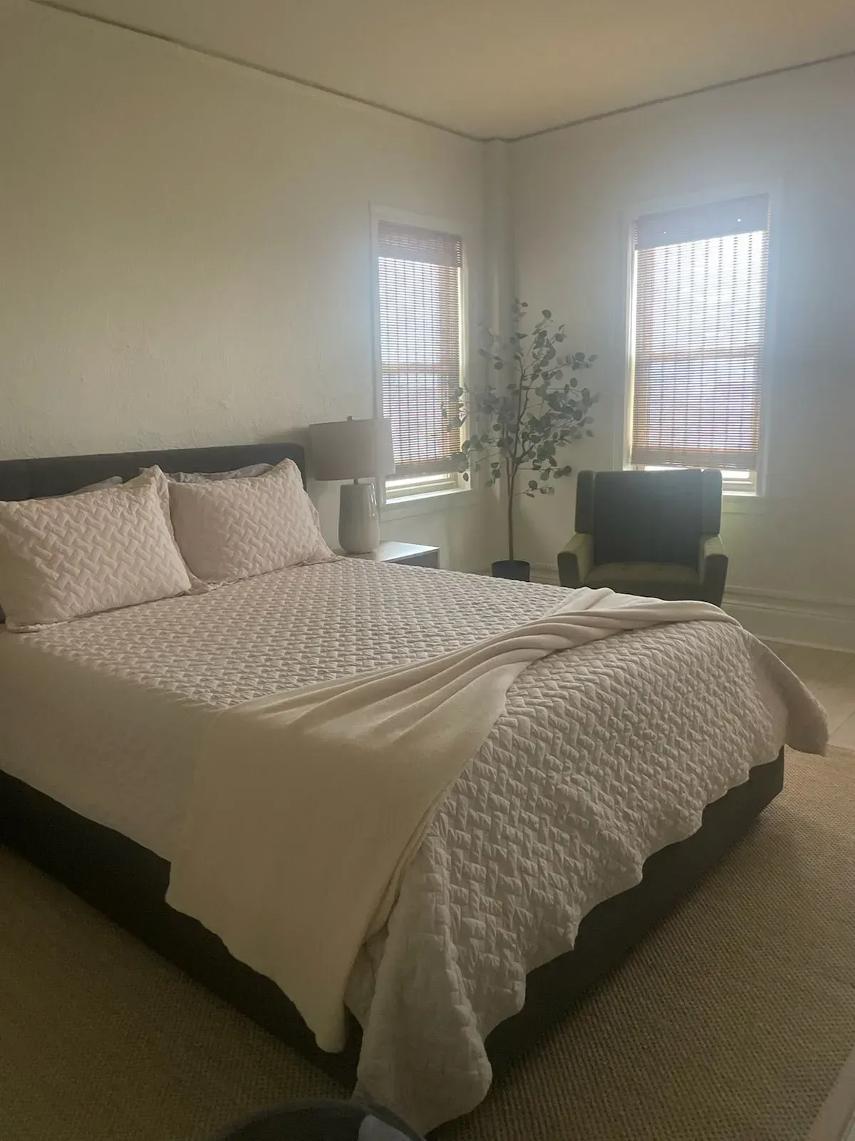A bedroom with a bed , chair , lamp and window.