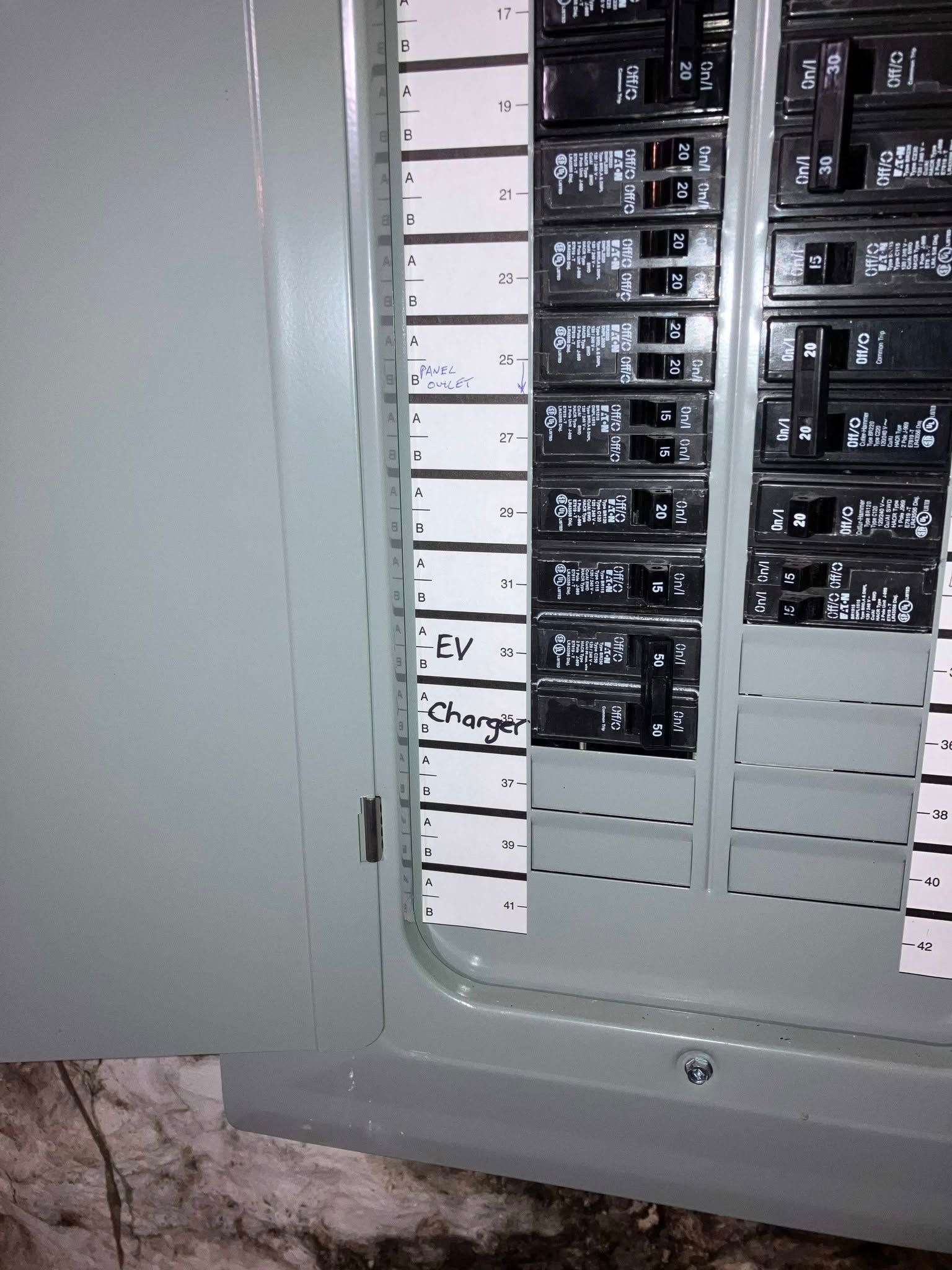 Open electrical breaker panel with rows of black circuit breakers and a partially visible labels column