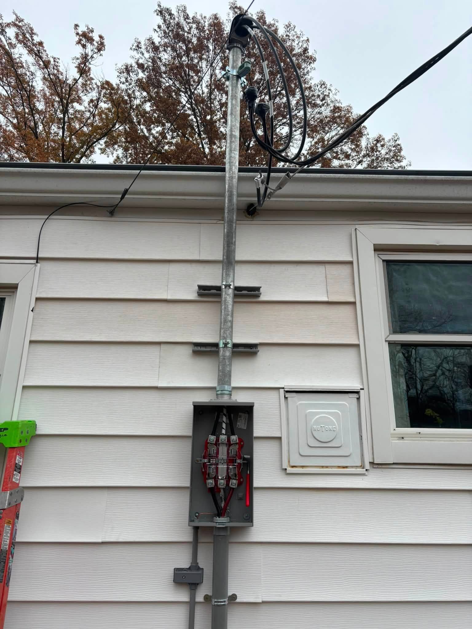 Electrical meter and service box mounted on a white house exterior with overhead power lines.