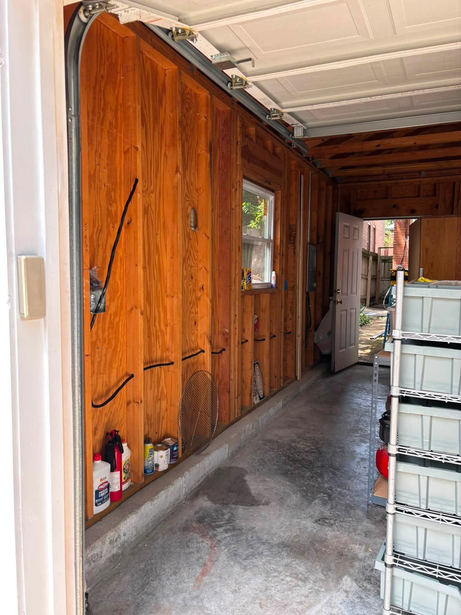 Wood-paneled garage wall with tools and stacked plastic bins along a narrow concrete walkway