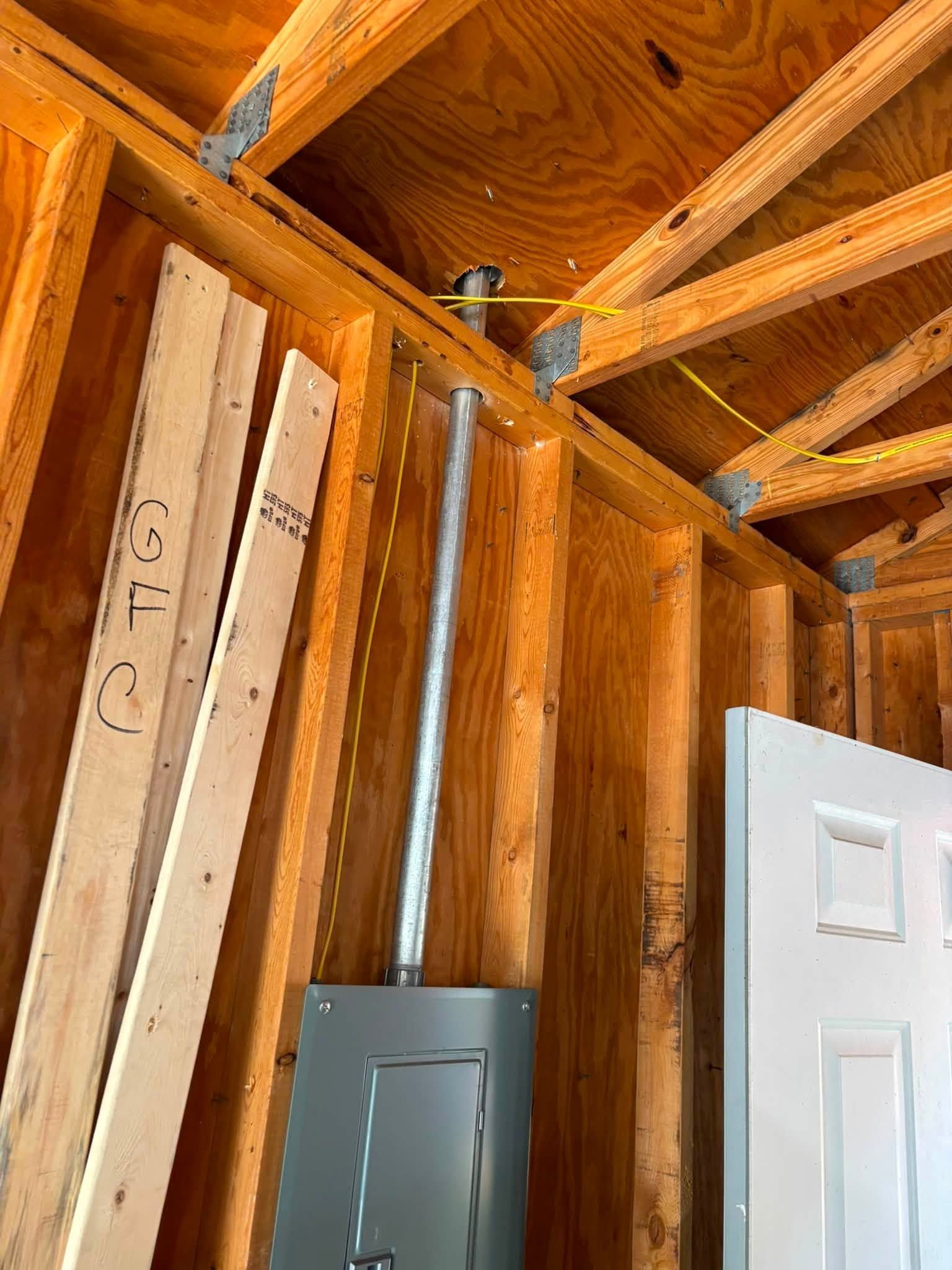 Interior wall framing with exposed wooden studs, ceiling joists, electrical panel, and open white door