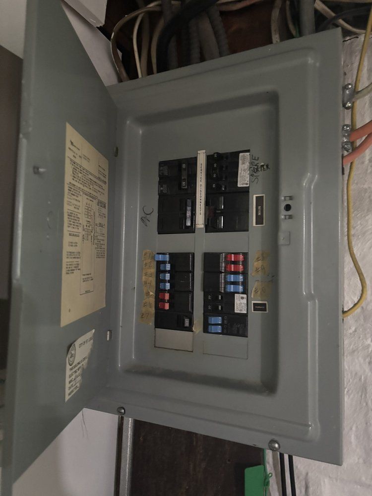 Open electrical breaker panel with multiple black, red, and blue circuit breakers.