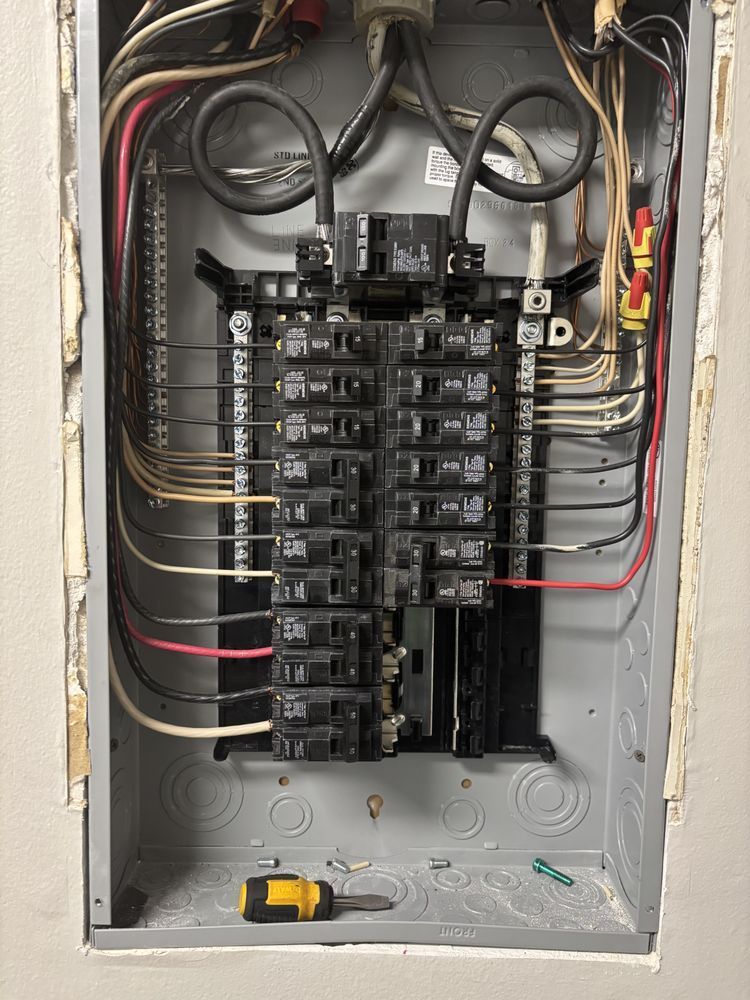 Open electrical breaker panel with wires and switches, yellow tool at the bottom.