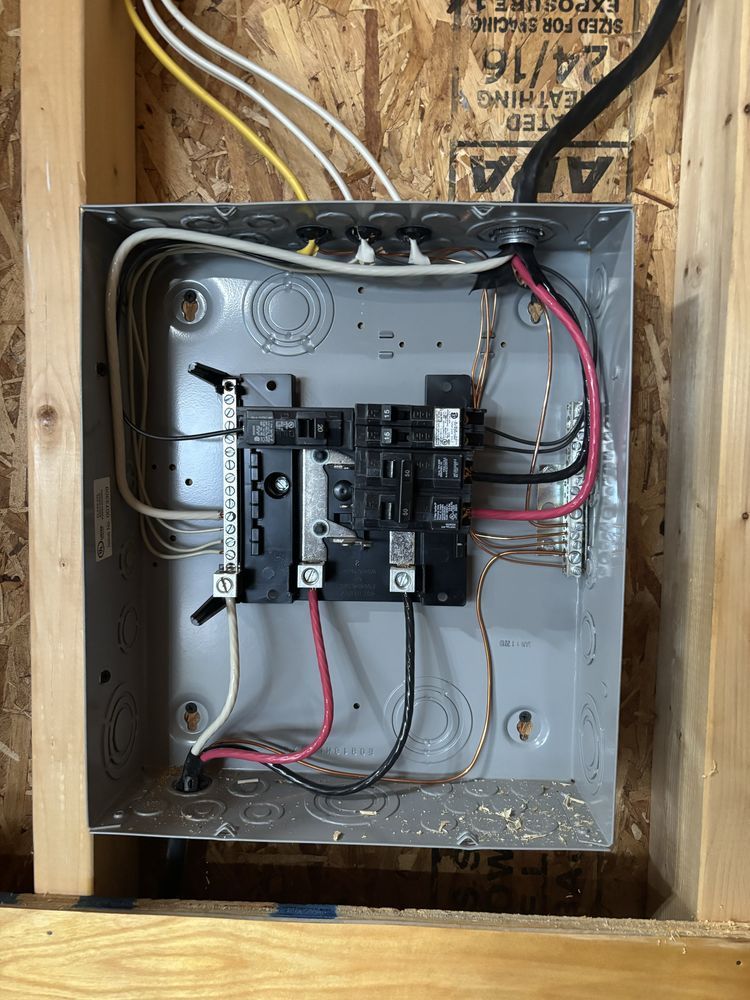 Open electrical breaker panel mounted in wooden framing with exposed wires.