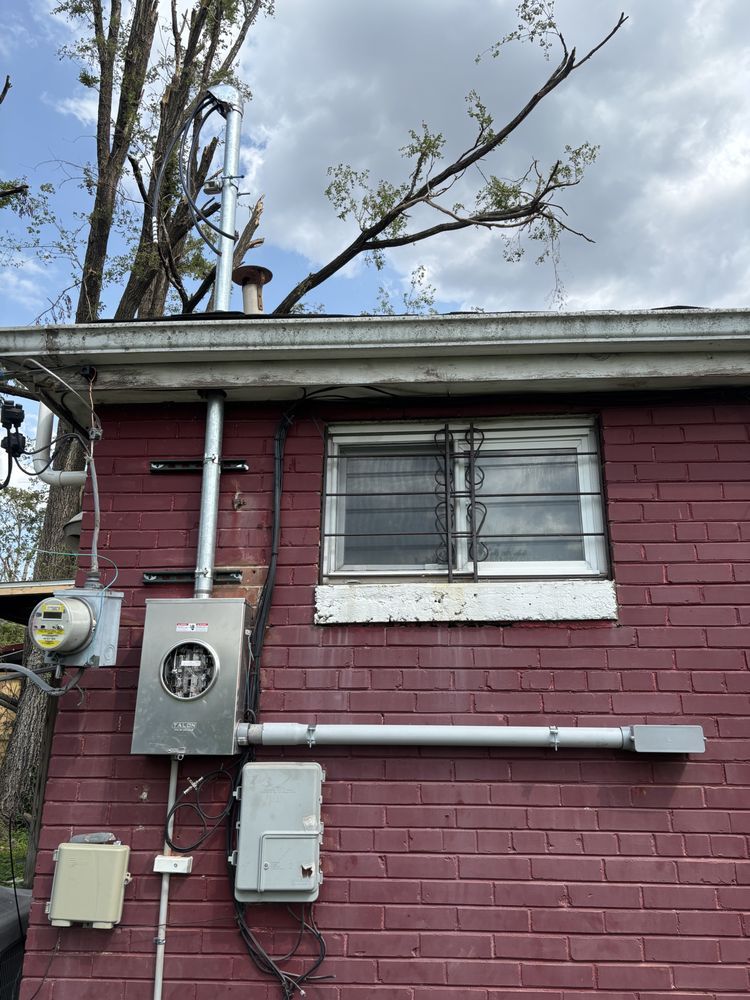 Red brick house wall with utility meters, white-trimmed window, and leafless tree branches above