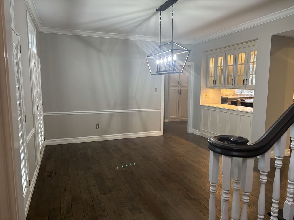 Empty dining room with dark hardwood floors, gray walls, white trim, and a hanging chandelier.