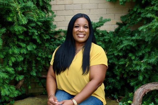 A woman in a yellow shirt is sitting on a bench in front of a tree.