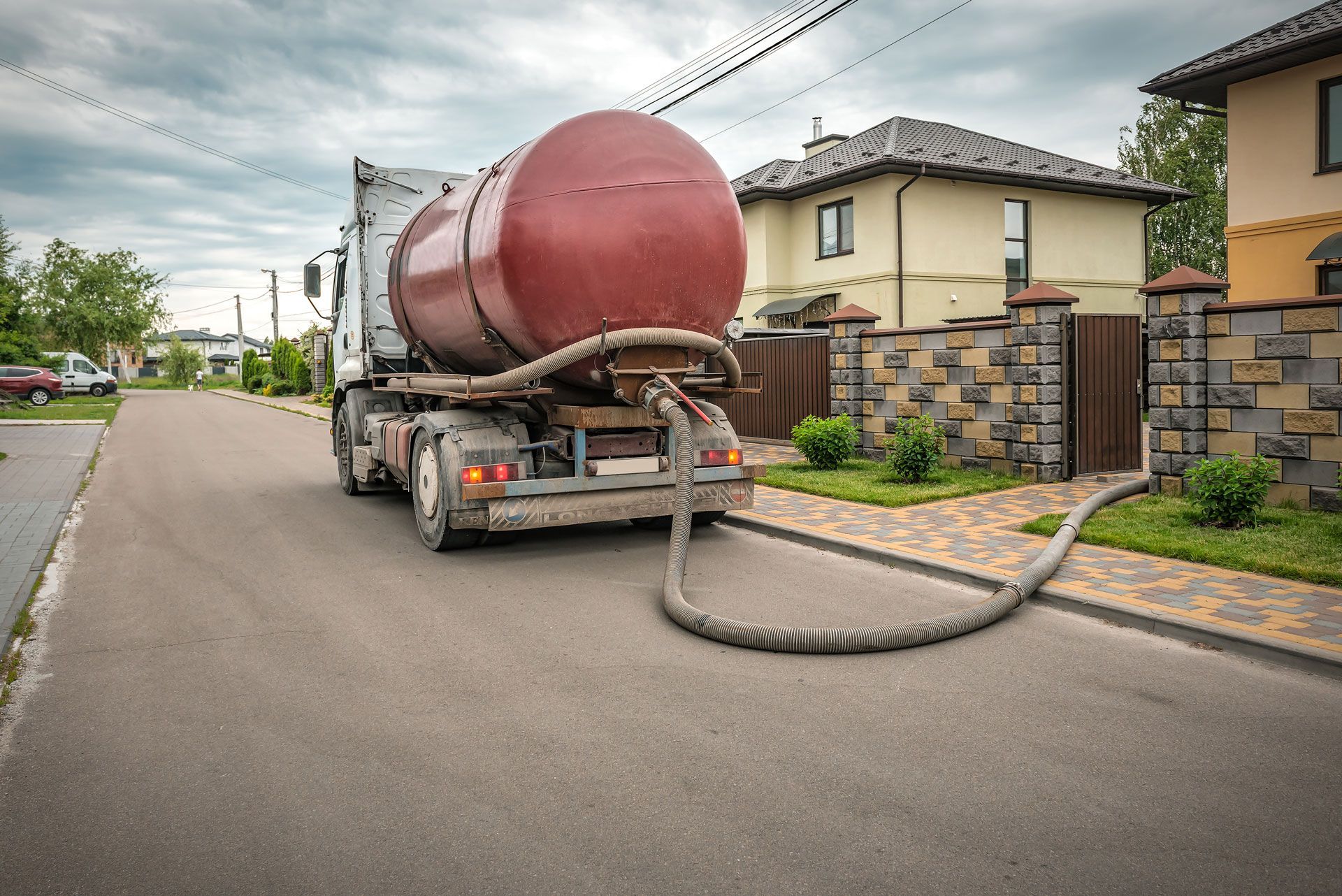 Septic tank truck parked on street, hose connected to a residential property.