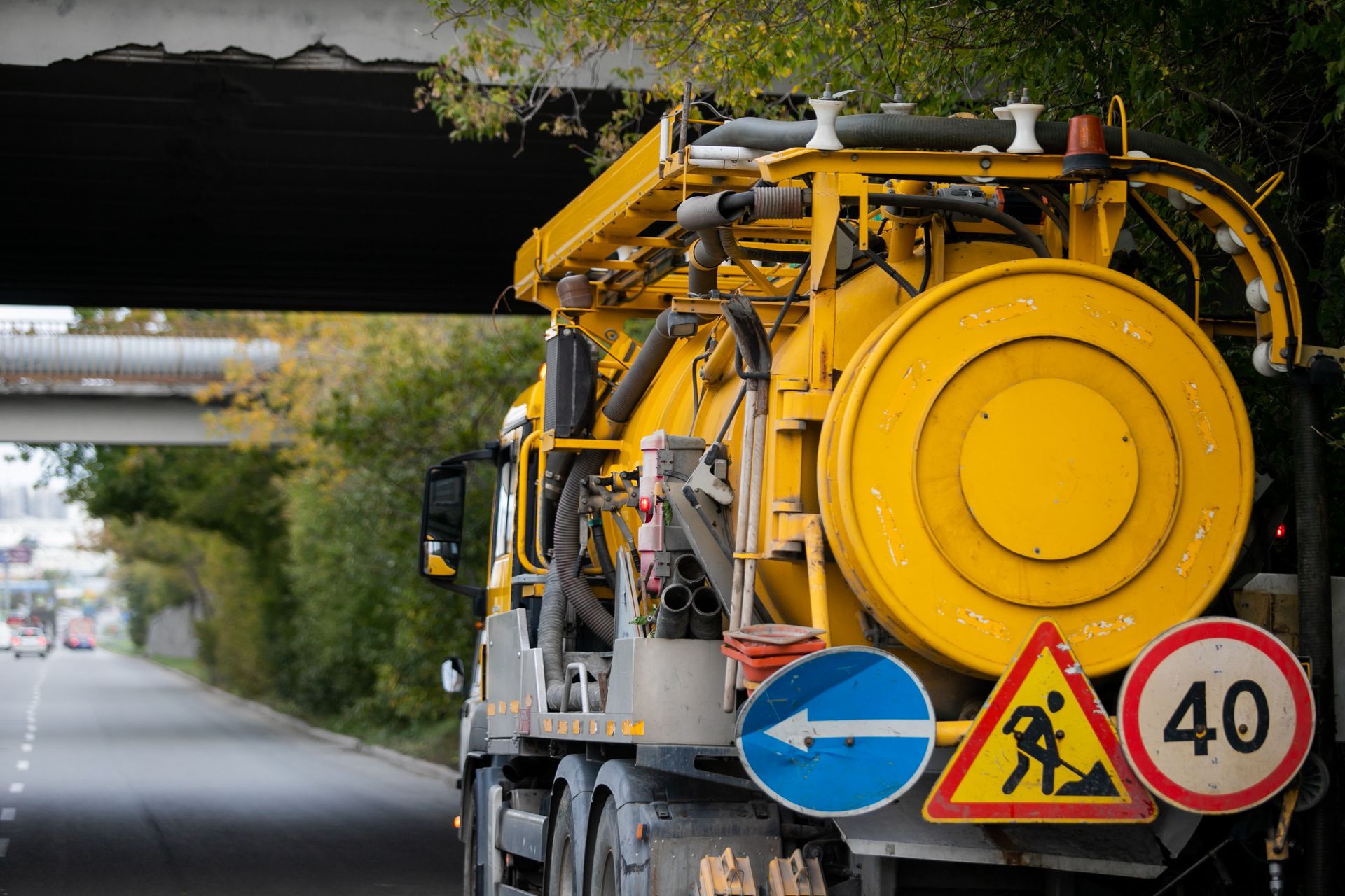 Yellow roadwork truck with warning signs on a highway, under a bridge.