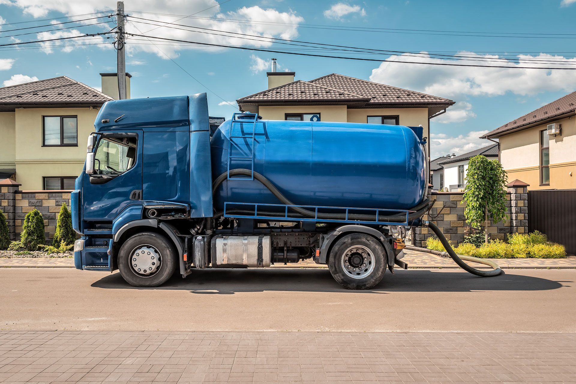 Blue septic tank truck parked on a residential street, hose extended towards unseen location.