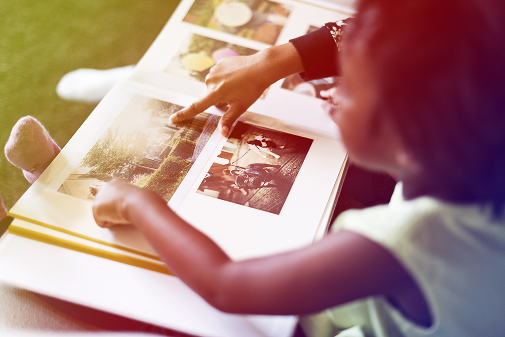 A child points at a photo in a photo album, bright lighting.