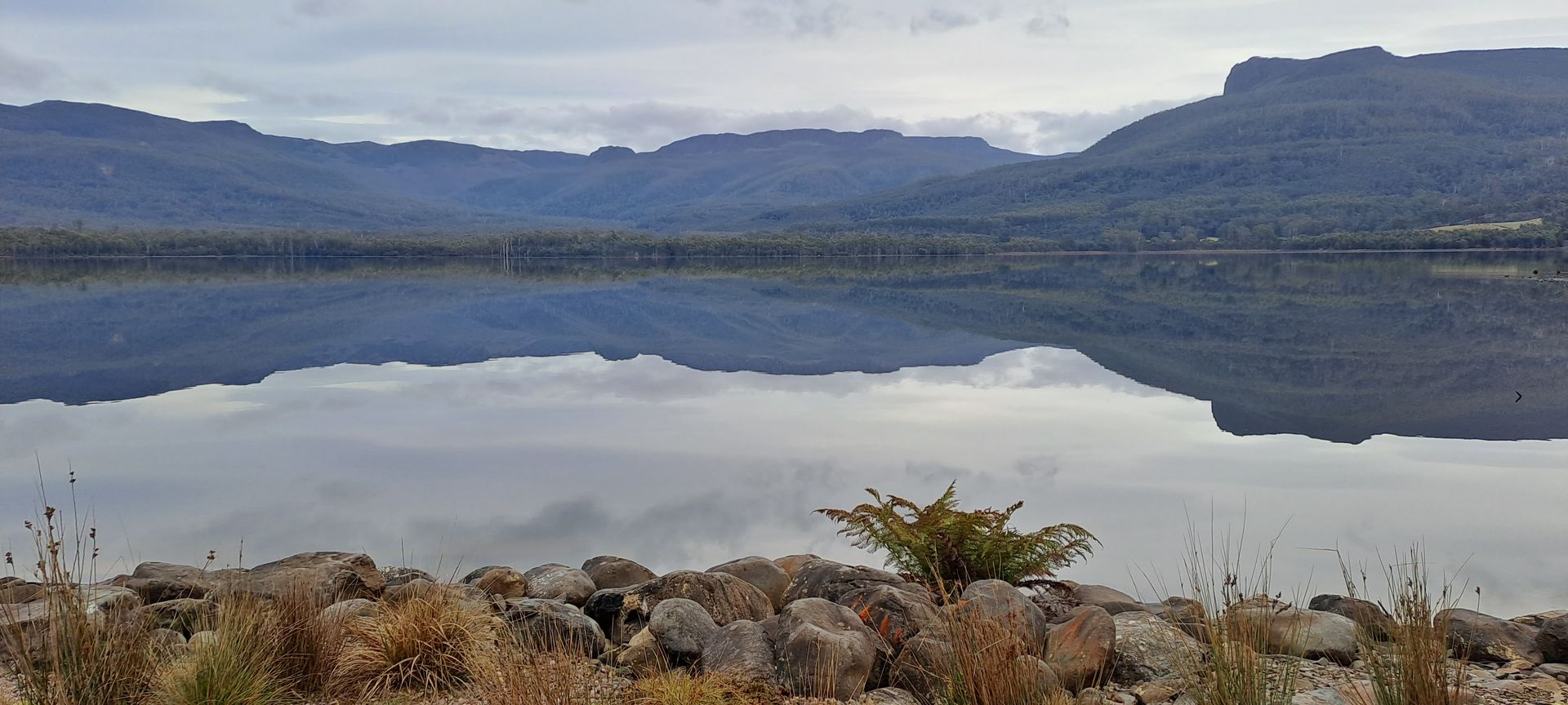 Calm lake reflects mountains and sky; rocks in foreground.