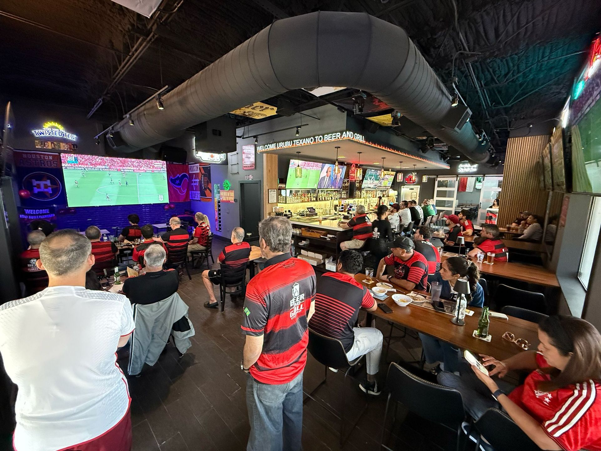 A group of people are sitting at tables in a restaurant watching a soccer game.