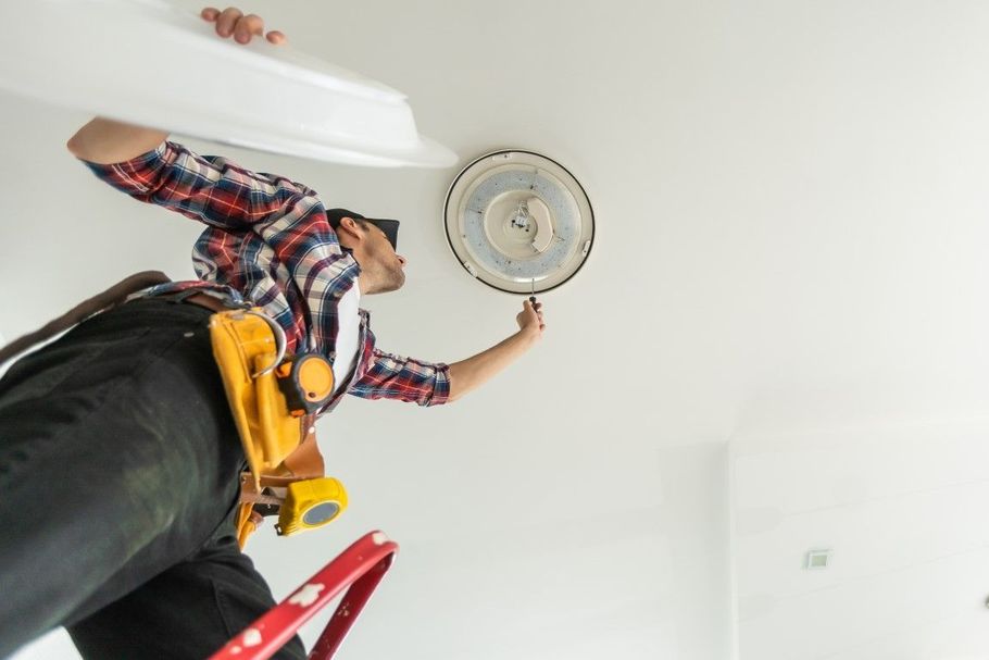 Worker installing a ceiling light while standing on a ladder, viewed from below