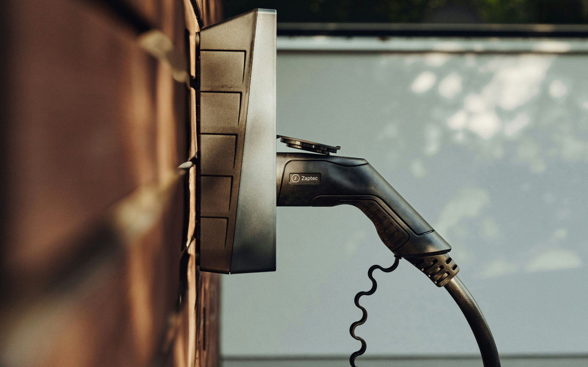 An electric vehicle charging plug connected to a wall-mounted charger outdoors