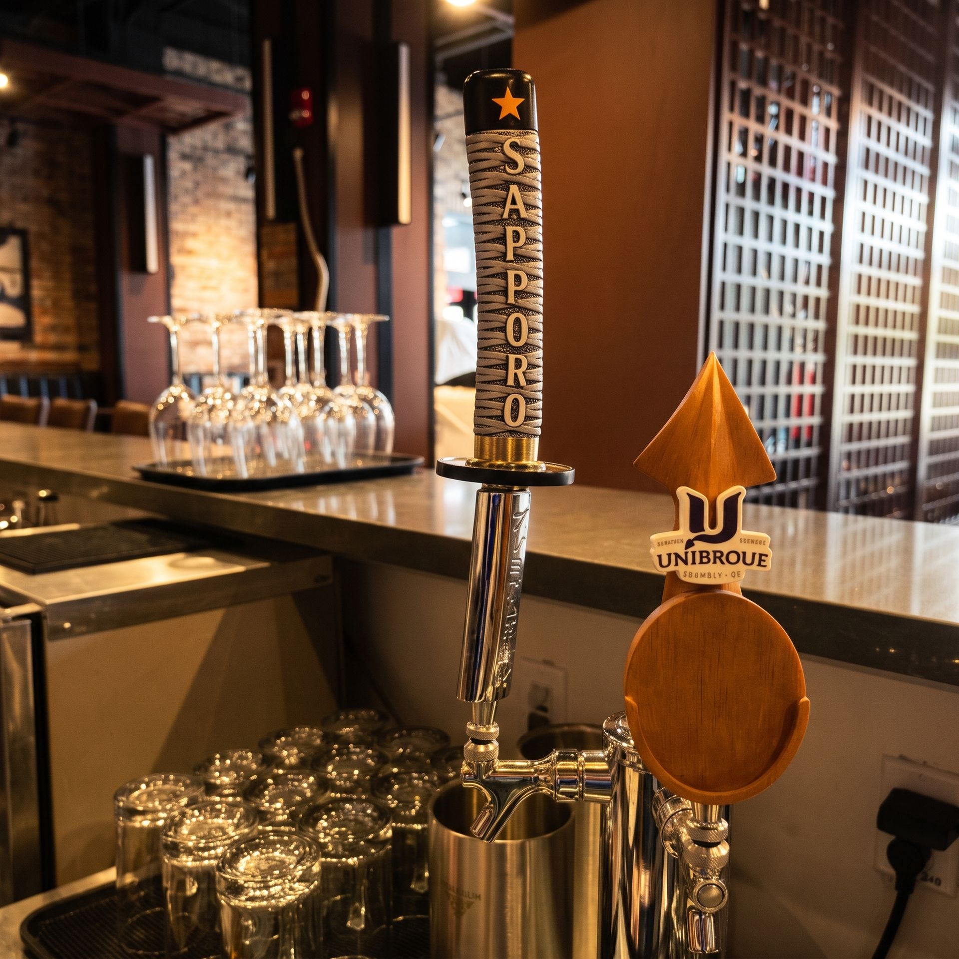 Beer tap labeled “San Pedro” at a bar, with rows of glassware on the counter.