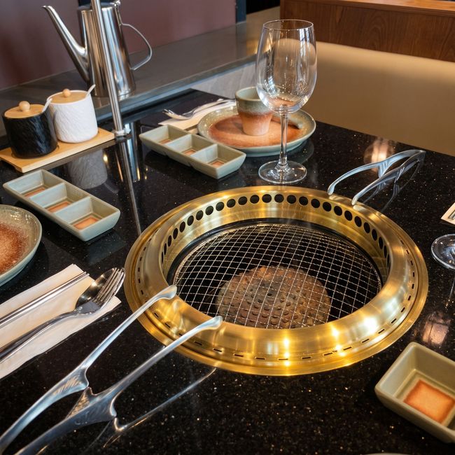 Black tabletop yakiniku grill with metal grates, sauces, chopsticks, and wine glasses in a restaurant