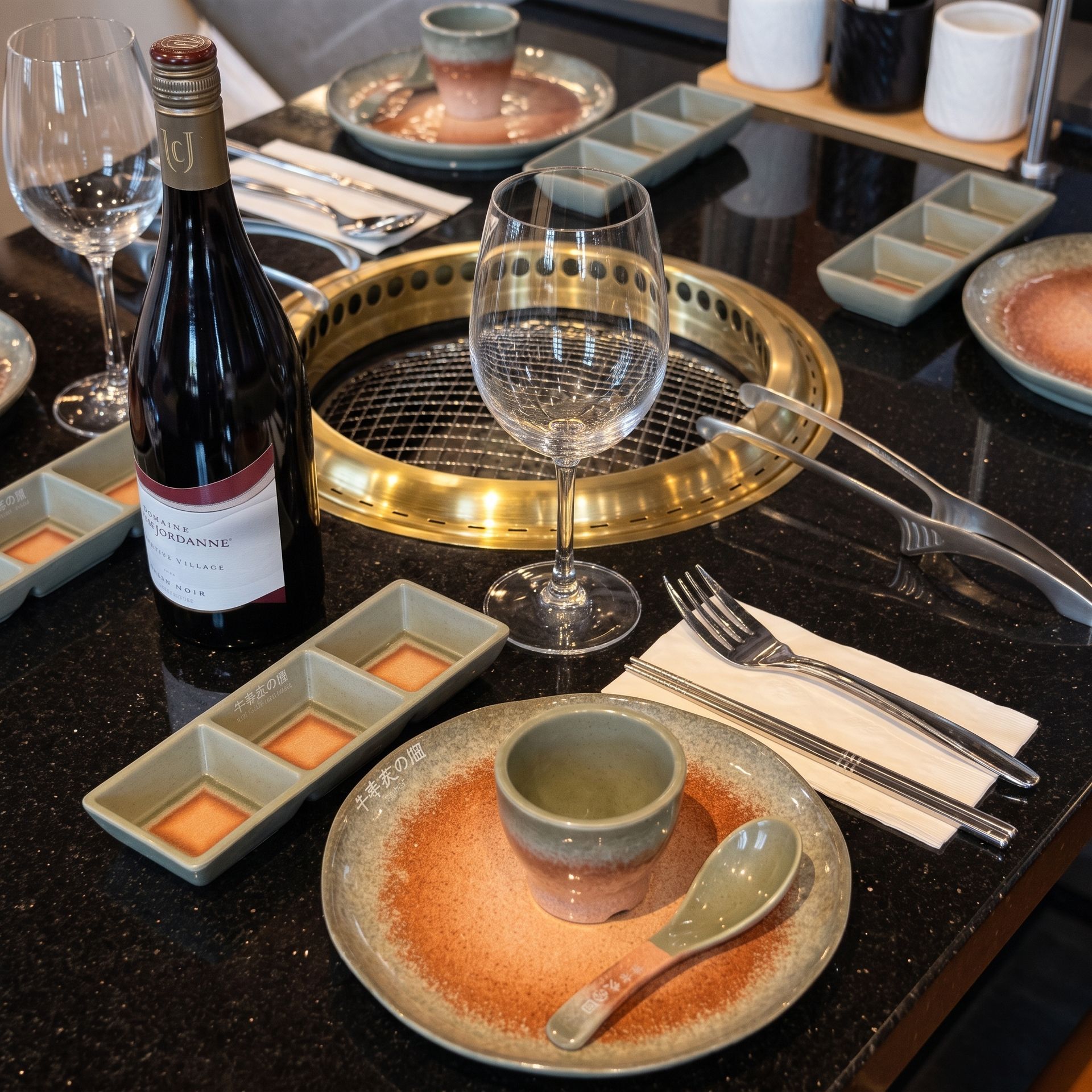 Elegant dining table with wine bottle, glasses, and place settings around a built-in grill.