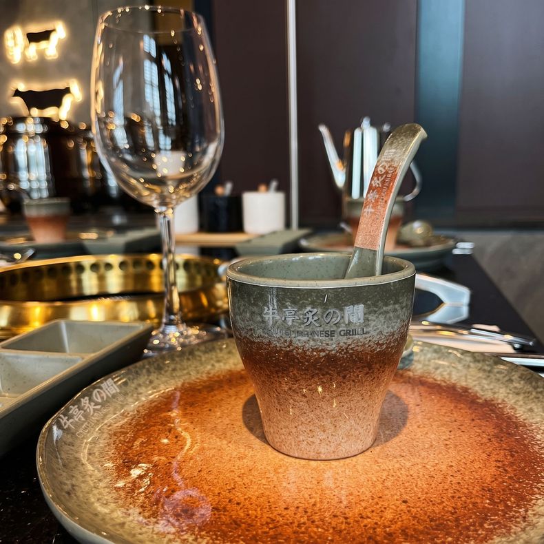 Copper-toned dessert bowl with a spoon, on a restaurant table beside a wine glass