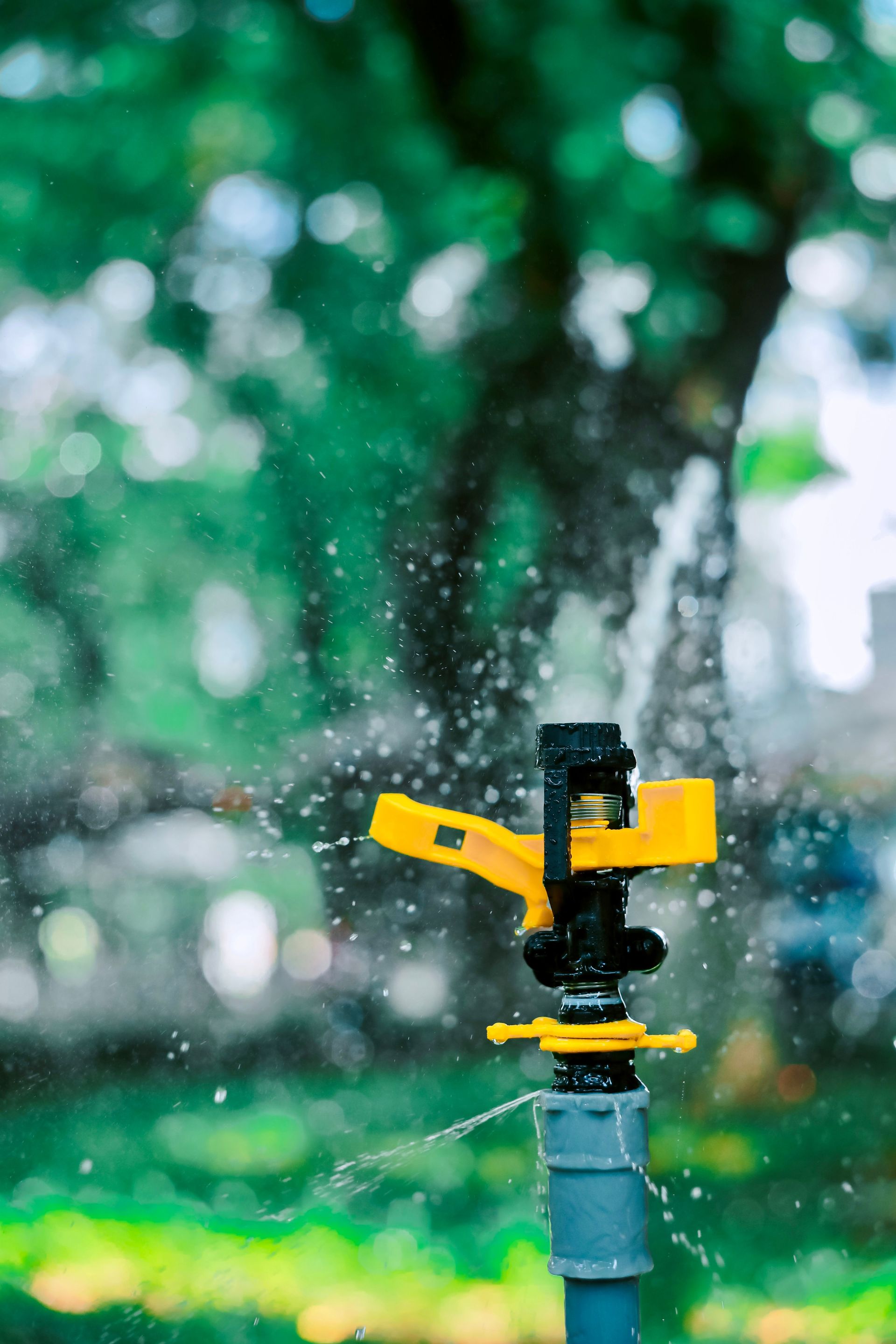 Yellow sprinkler spraying water in a blurred green garden background
