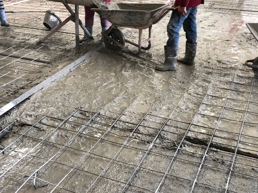 A Man Is Pouring Concrete Into A Wheelbarrow On A Construction Site — Concept Concreting NSW In Figtree, NSW