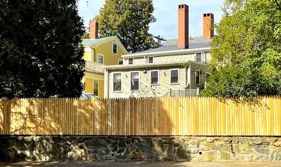 A wooden fence surrounds a stone wall in front of a house.