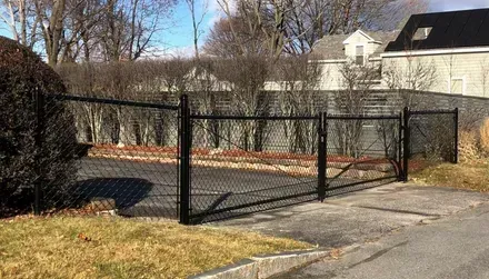 A black chain link fence surrounds a driveway in front of a house.