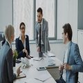 Business meeting around a conference table, with one man speaking and others listening in a bright office.